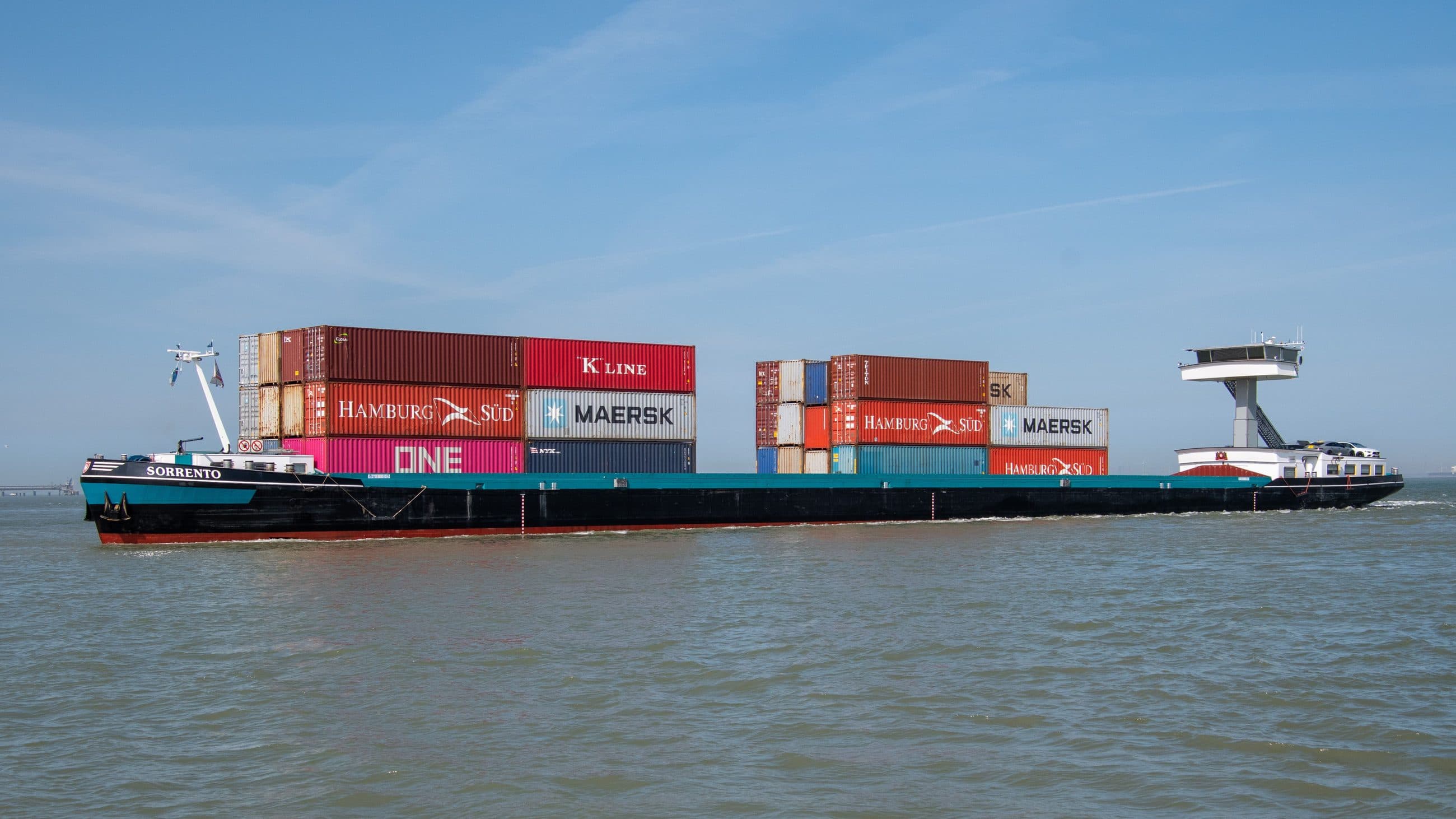 Barge fluviale en navigation chargée de conteneurs maritimes empilés sur deux hauteurs